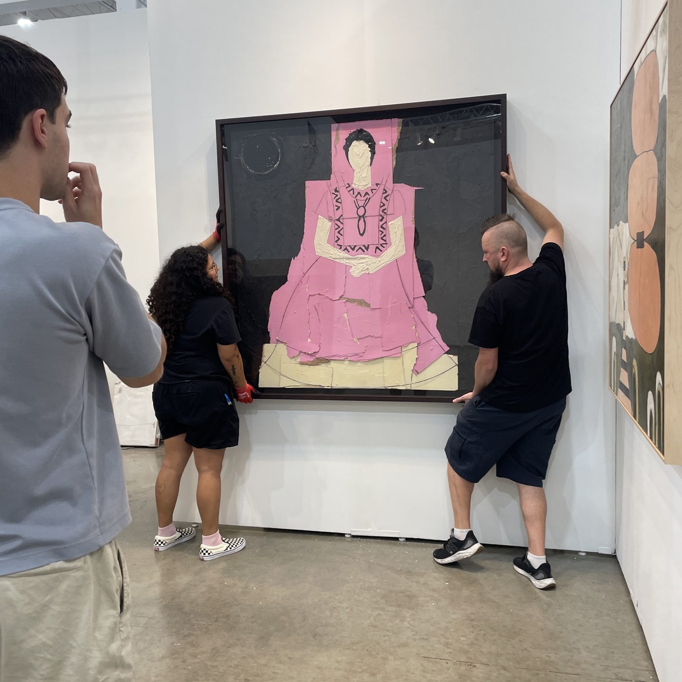 A three-person team carefully lifting a large framed artwork into place